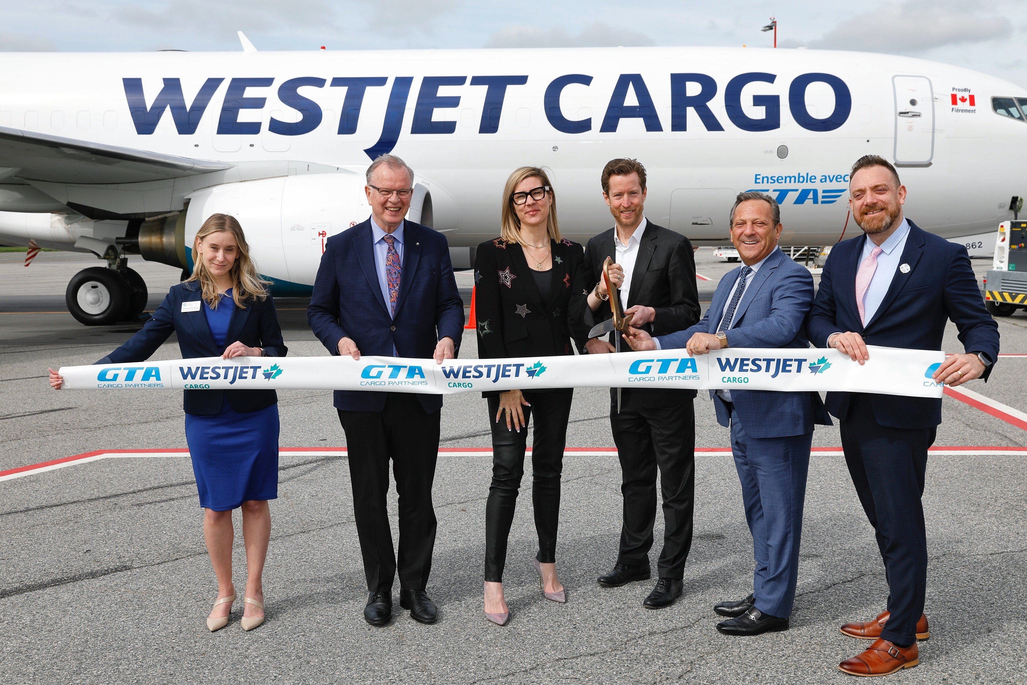 Five individuals standing in front of WestJet Cargo airplane cutting ribbon