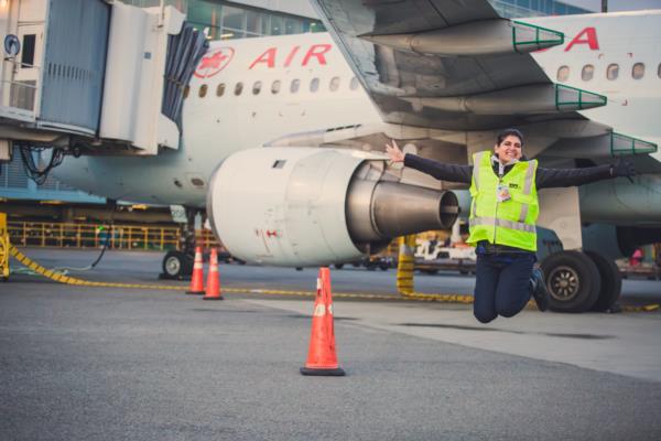 Dayah, a YVR employee with a big smile jumps with her arms outstretched outside on the airfield. 