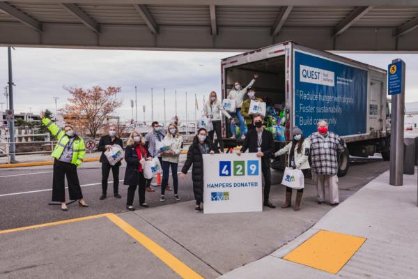 A group of people stand socially distanced, with masks on in front of a truck with all the hamper bags inside