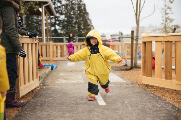 A little girl in a yellow rain suit runs towards the camera 