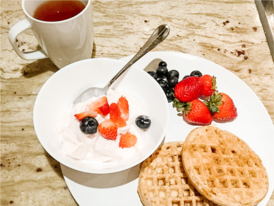 Petit déjeuner de yaourt, myrtilles, fraises et gaufres avec une tasse de thé en haut à gauche.