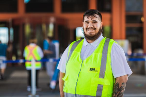 A worker at the Richmond Vaccination Site is smiling in front of the entrance