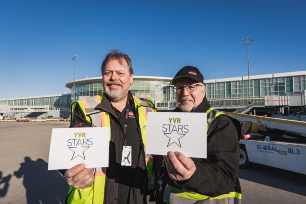 Photo de Ted et Glenn posant côté piste avec le panneau Étoiles d’YVR.