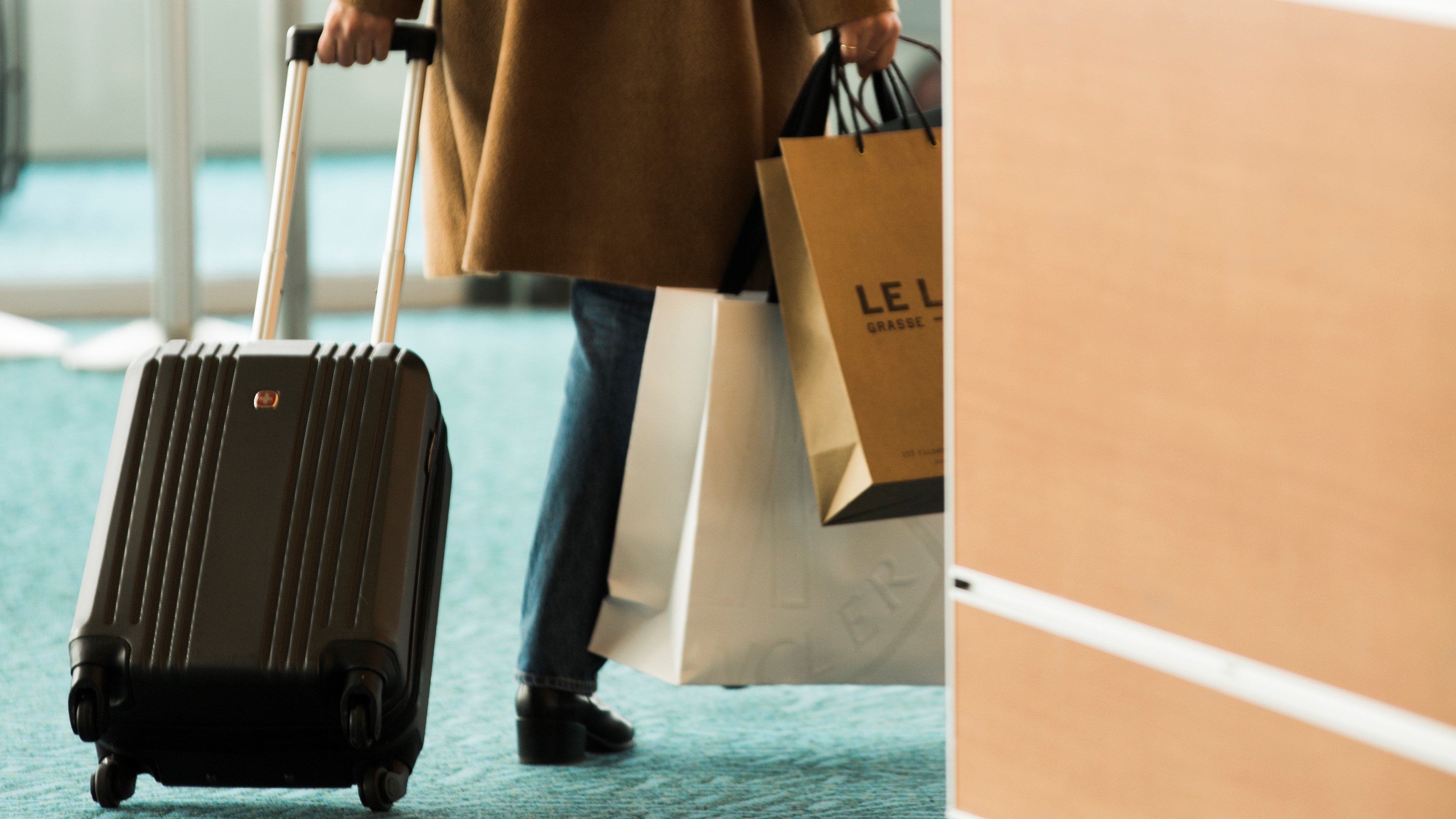 Person walking in the terminal with a carry-on suitcase and some duty free bags.