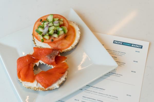 A bagel with wild salmon, tomatoes, cucumbers, onions and a menu underneath plate