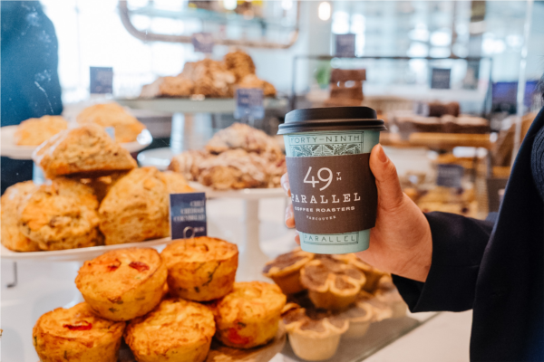 Person holding 49th Parallel coffee cup in front of pastry bar