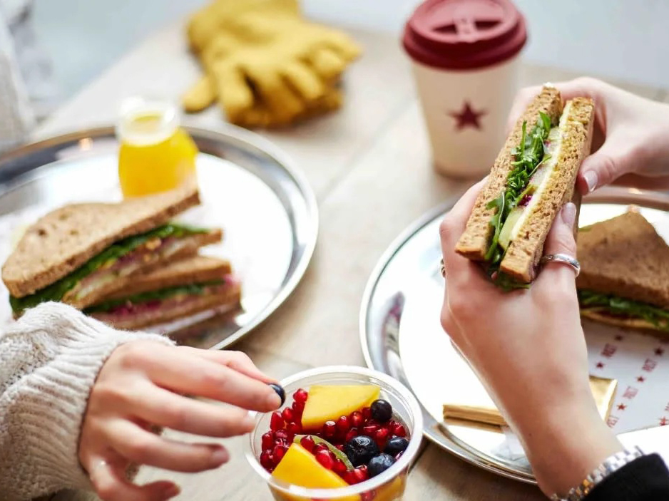 Hands of two people eating sandwiches and fruit cup