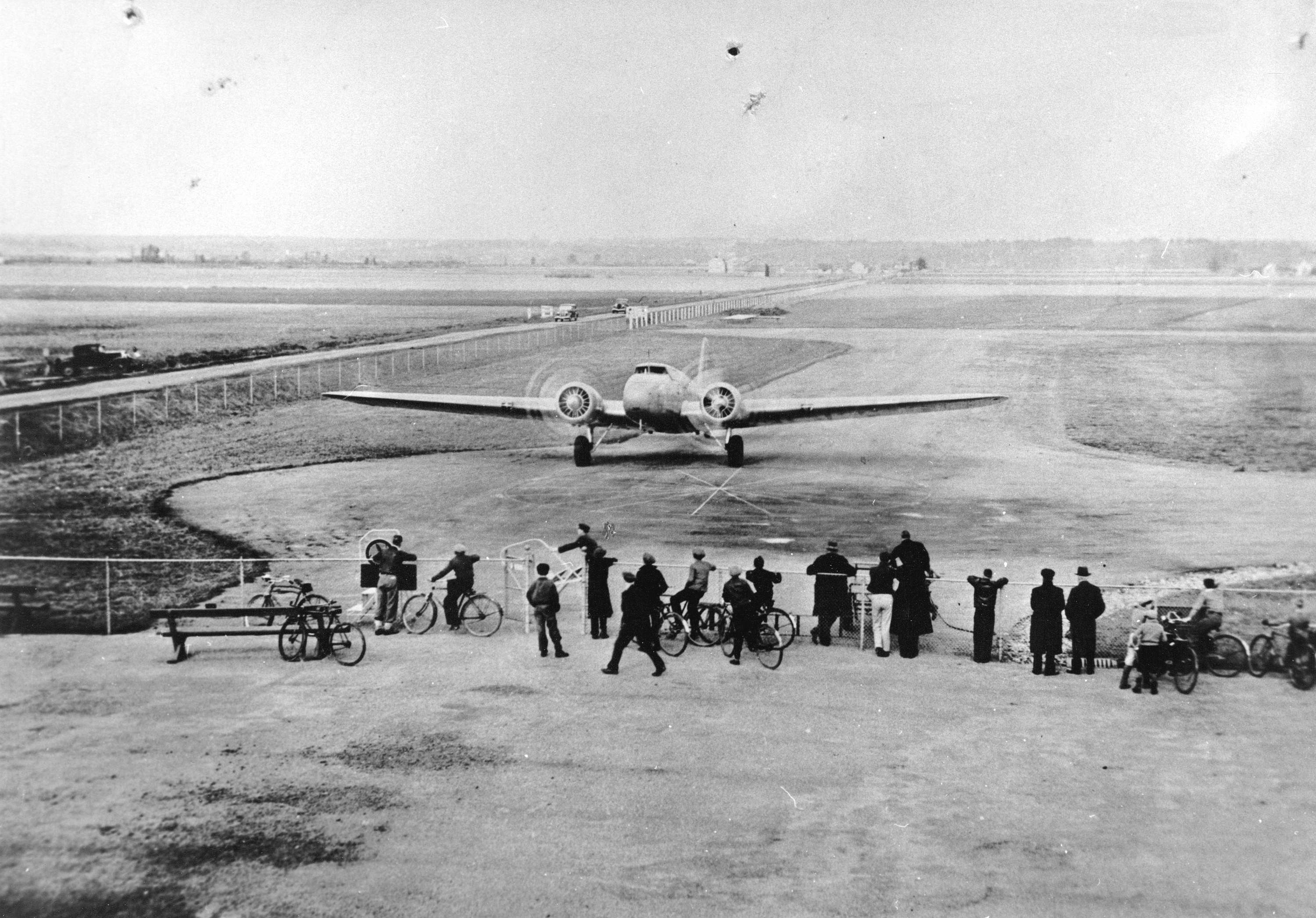 Photo of a group of people standing in front of an airplane taking off on a runway